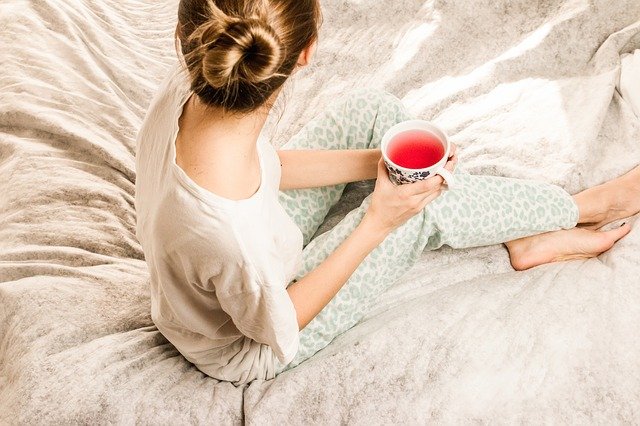 Žena v pyžame s čajom v ruke sediaca v posteli.jpg